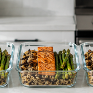 A row of glass meal prep containers filled with balanced healthy meals on a clean kitchen counter.