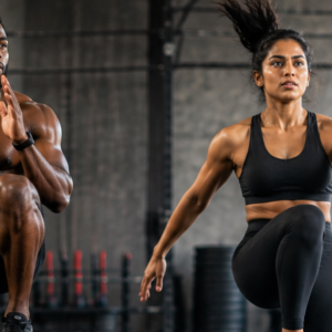 A Black man and a South Asian woman doing high-knee jumps during a HIIT workout in a gym