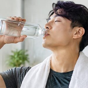 Woman drinking water from a glass bottle at home, staying hydrated as part of a weight loss and fitness routine